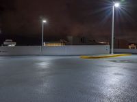 a parking lot at night with lights from above the buildings in the background, a yellow rail line and some blacktop