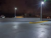 a parking lot at night with lights from above the buildings in the background, a yellow rail line and some blacktop