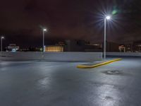 a parking lot at night with lights from above the buildings in the background, a yellow rail line and some blacktop