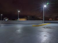 a parking lot at night with lights from above the buildings in the background, a yellow rail line and some blacktop