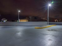 a parking lot at night with lights from above the buildings in the background, a yellow rail line and some blacktop