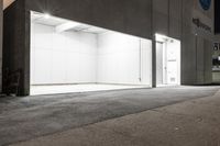 a closed parking garage with lights on at night, outside, and street scene in a commercial city area