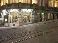 a cobblestone road in front of a building that has windows that have lights on