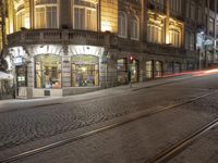 a cobblestone road in front of a building that has windows that have lights on