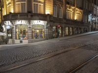 a cobblestone road in front of a building that has windows that have lights on