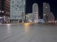 a square in the middle of a large city with people walking on it at night