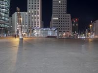 a square in the middle of a large city with people walking on it at night
