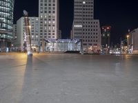 a square in the middle of a large city with people walking on it at night