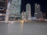 a square in the middle of a large city with people walking on it at night