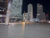 a square in the middle of a large city with people walking on it at night