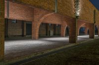 an open courtyard with three brick archways lit up at night with street lights on