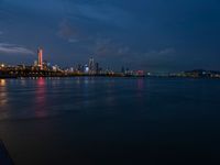 the view from an embankment of city skylines and a harbor at night as seen from across the water