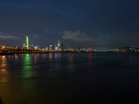 the view from an embankment of city skylines and a harbor at night as seen from across the water