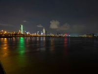 the view from an embankment of city skylines and a harbor at night as seen from across the water