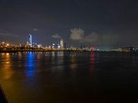 the view from an embankment of city skylines and a harbor at night as seen from across the water