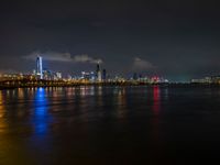 the view from an embankment of city skylines and a harbor at night as seen from across the water