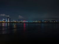 the view from an embankment of city skylines and a harbor at night as seen from across the water