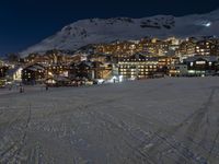 a ski resort at night with snowy slopes and houses on top of the mountain in the background