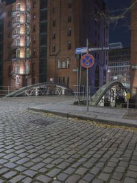 a street bridge that is over some buildings on a street at night, with some leaves all around the walkway