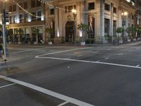 a street with a light at the corner and a building to the side and some lights above the street