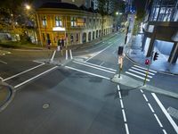 a street has two buildings at night and lights at red traffic light with people walking across the road