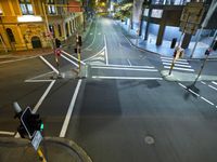 a street has two buildings at night and lights at red traffic light with people walking across the road