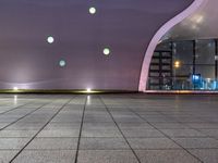 a tiled floor with purple lighting at night and a building in the background with some windows