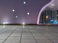 a tiled floor with purple lighting at night and a building in the background with some windows