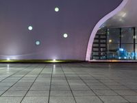 a tiled floor with purple lighting at night and a building in the background with some windows