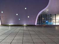 a tiled floor with purple lighting at night and a building in the background with some windows