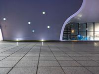 a tiled floor with purple lighting at night and a building in the background with some windows