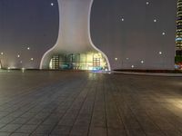 a clock tower in a building at night in an empty space, with buildings in the background