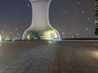 a clock tower in a building at night in an empty space, with buildings in the background