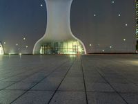 a clock tower in a building at night in an empty space, with buildings in the background