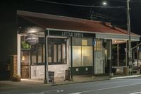 a street at night with a cafe in the corner and a bus coming out of it