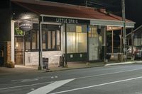 a street at night with a cafe in the corner and a bus coming out of it