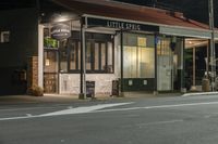 a street at night with a cafe in the corner and a bus coming out of it