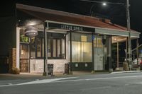 a street at night with a cafe in the corner and a bus coming out of it