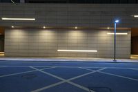 a parking lot near a brick wall with illuminated lines on it at night with street lights