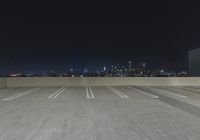 an empty parking lot with several lights on top of it at night with buildings in the background