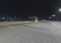 an empty parking lot with several lights on top of it at night with buildings in the background