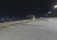 an empty parking lot with several lights on top of it at night with buildings in the background