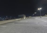 an empty parking lot with several lights on top of it at night with buildings in the background