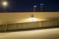 an empty road near two tall buildings with street lamps in the middle of it at night