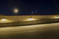 an empty road near two tall buildings with street lamps in the middle of it at night