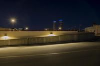 an empty road near two tall buildings with street lamps in the middle of it at night