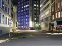 an empty city street with cars parked along it at night, with buildings in the background