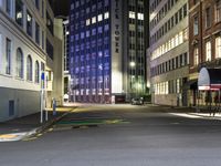 an empty city street with cars parked along it at night, with buildings in the background