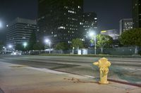 a yellow fire hydrant in front of buildings at night on the road between two street lights