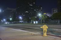 a yellow fire hydrant in front of buildings at night on the road between two street lights